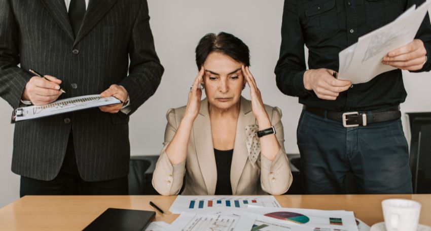 A woman is holding her head in front of a group of business people.